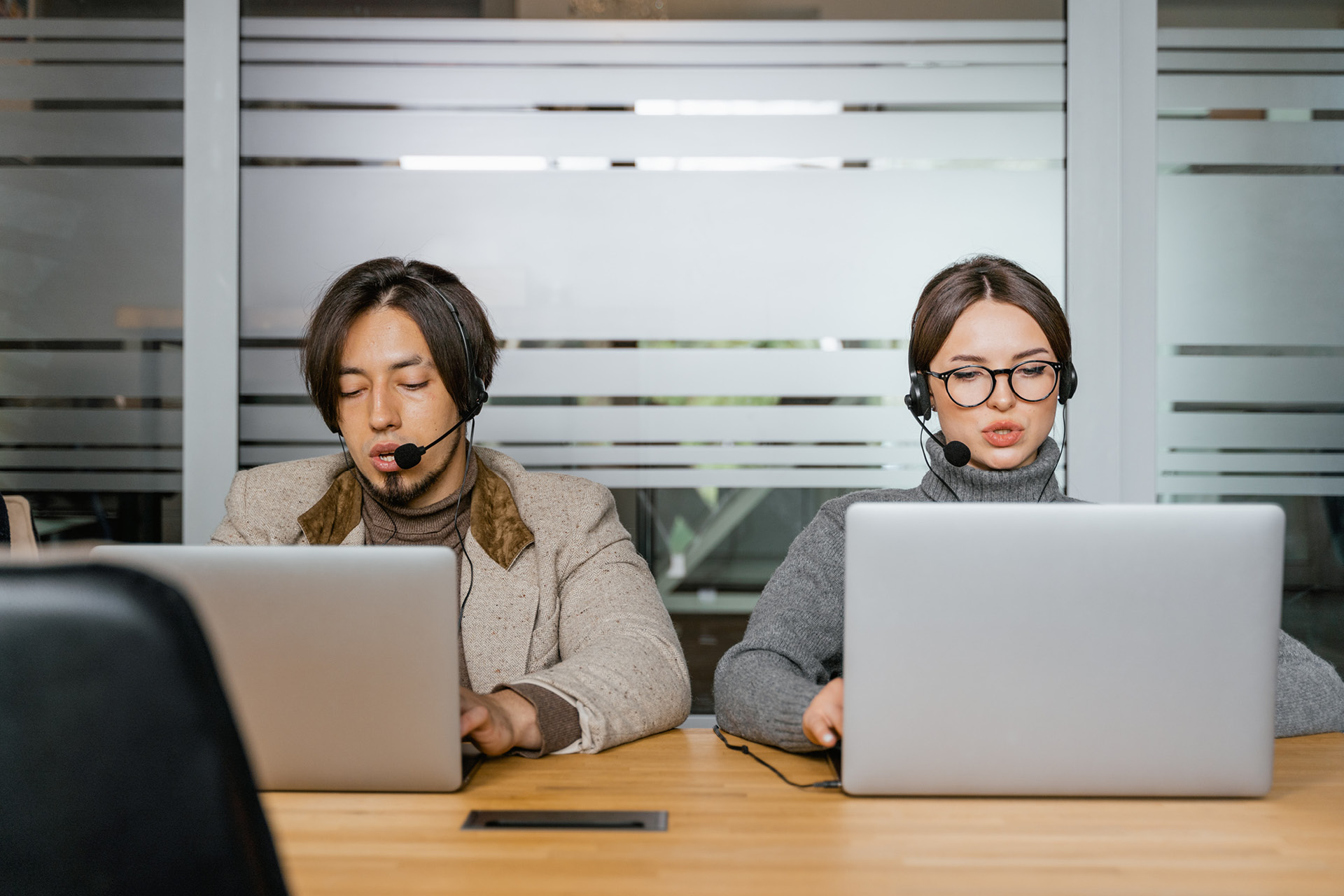 Ein Mann und eine Frau mit Headphone vor ihrem Laptop beim Simultandolmetschen.